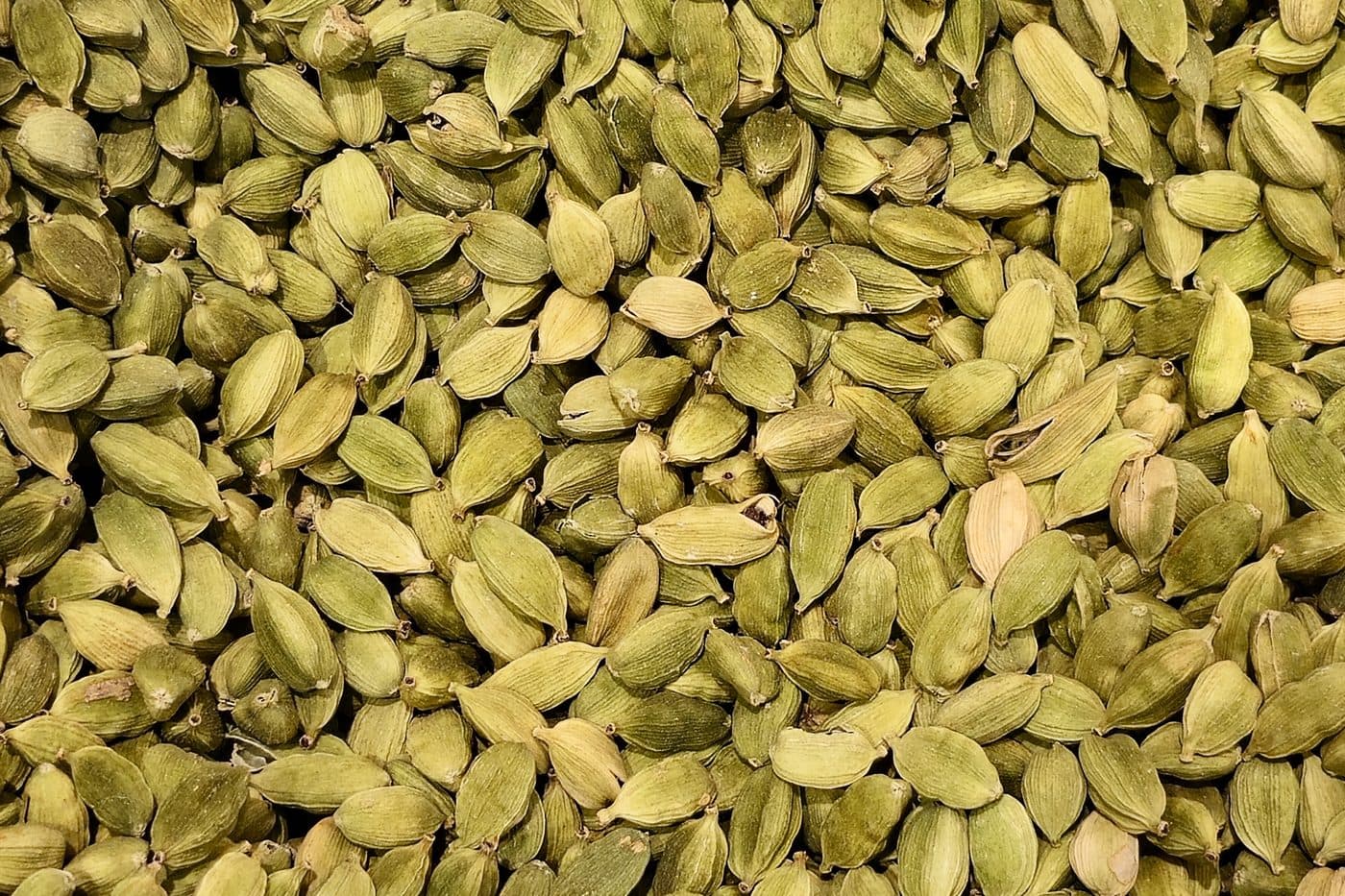 Green cardamom capsules in a sizing sieve with graded samples in small dishes