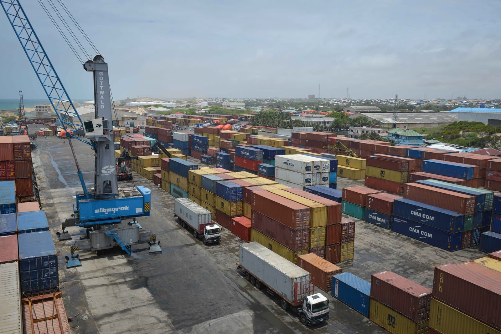 Stacked containers and a gantry crane at the terminal, trucks queuing along the yard for loading