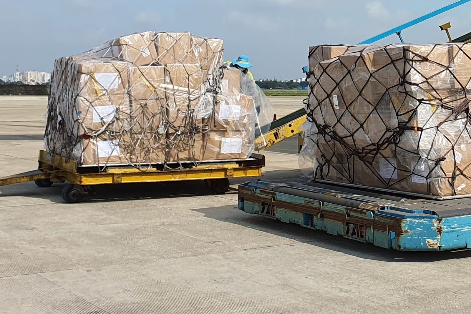 Cartons built into netted air cargo pallets on the apron, waiting beside the aircraft loader