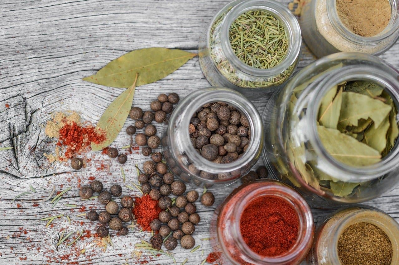 Whole and dried spices arranged in labelled sample jars on a light surface