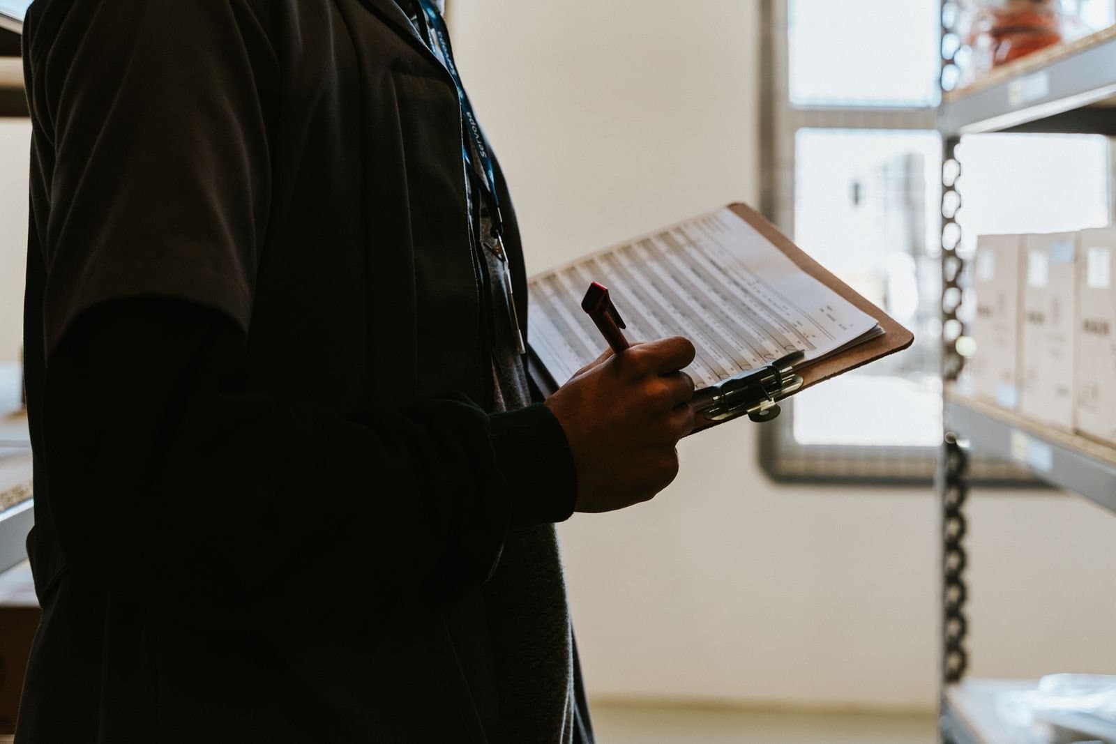 Warehouse supervisor checking stored stock against a stock record on a clipboard or tablet