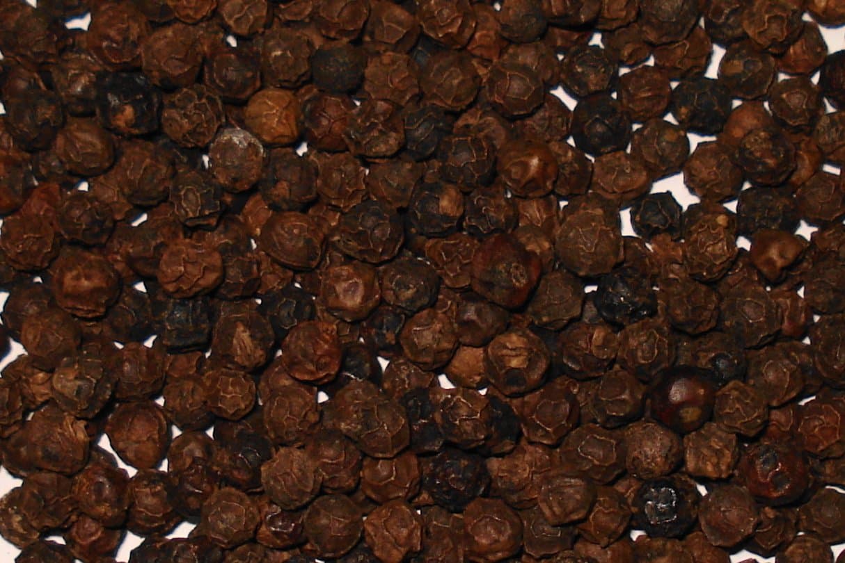 Dried black peppercorns being scooped from a sack into a measuring cylinder