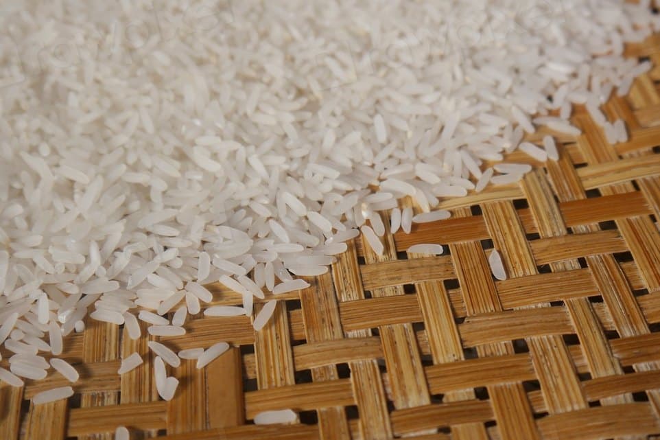 Cleaned milled white rice spilling across a woven bamboo mat