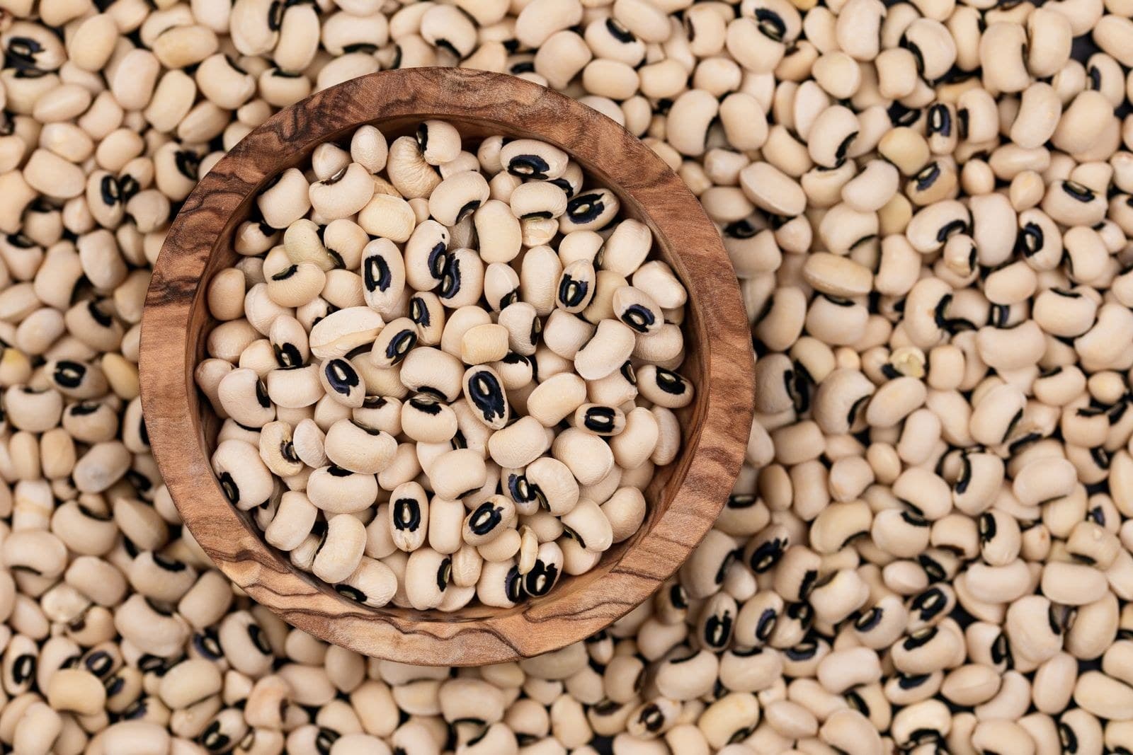 A wooden bowl of black-eyed cowpeas set in a bed of the same beans, seen from above