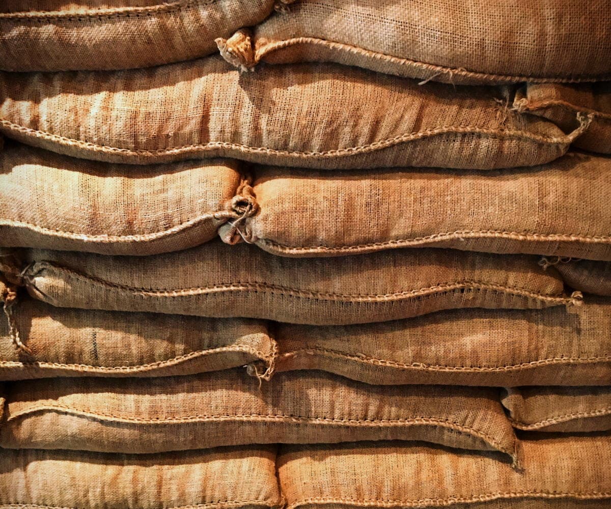 Filled jute sacks stitched closed and stacked in rows, seen along the sewn mouths