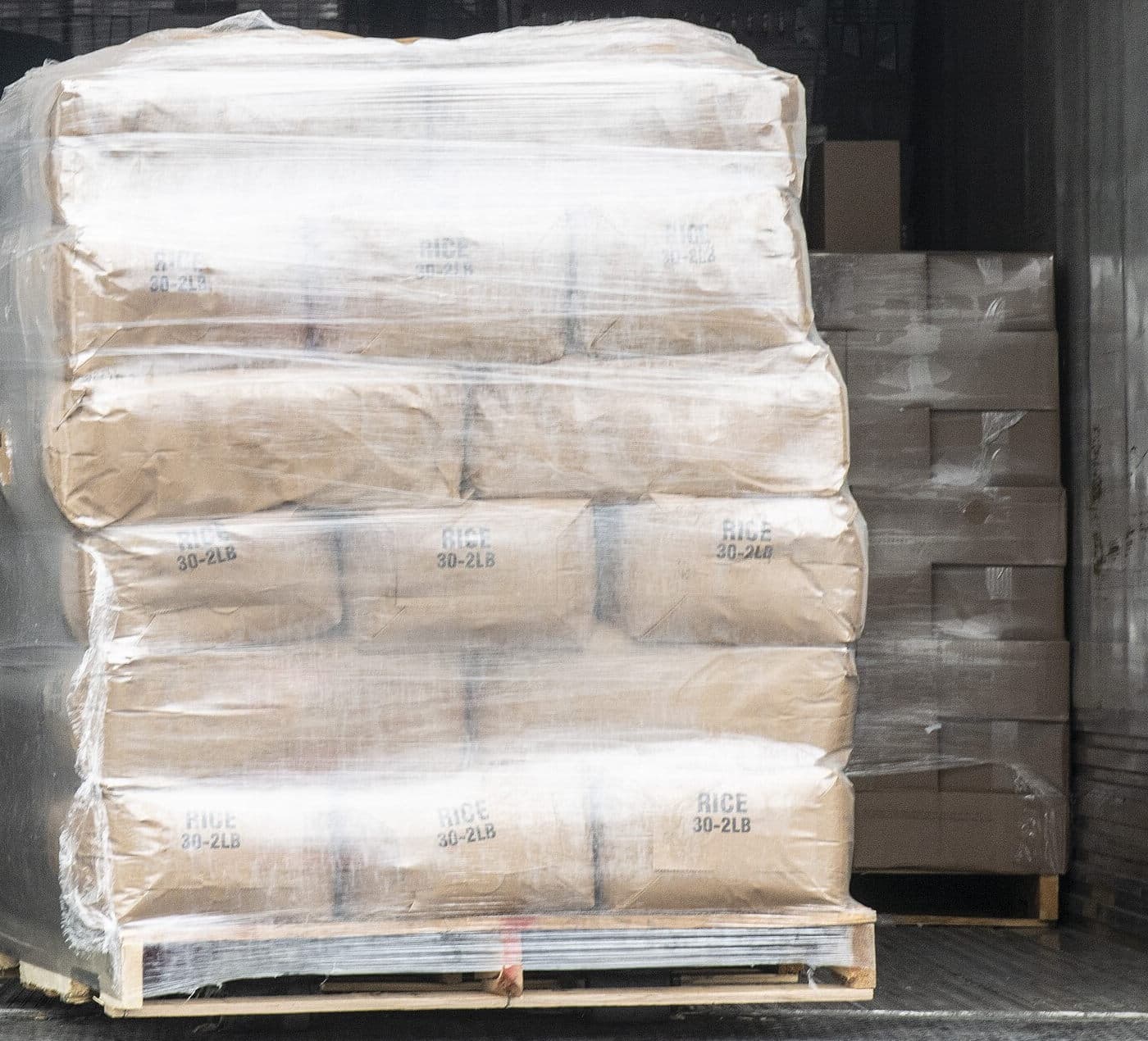 A wrapped pallet of bagged rice standing in the back of a delivery truck, a second load behind it