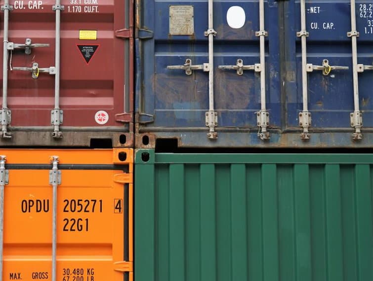 The closed doors of stacked shipping containers, locking bars down and the cargo markings showing