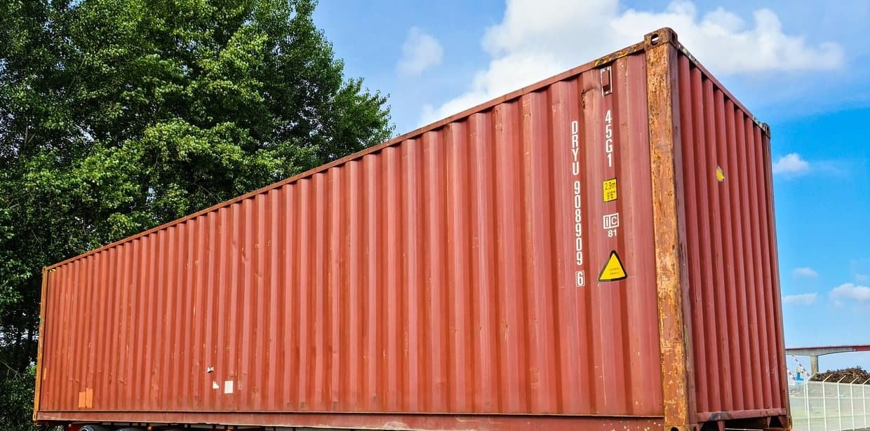 A shipping container standing loaded on a trailer under open sky